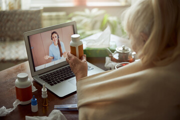 Old woman holding pills and talking with doctor though video call