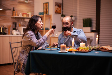 Couple toasting with wine glasses during romantic dinner. Relax happy people clinking, sitting at table in kitchen, enjoying the meal, celebrating anniversary in the dining room.