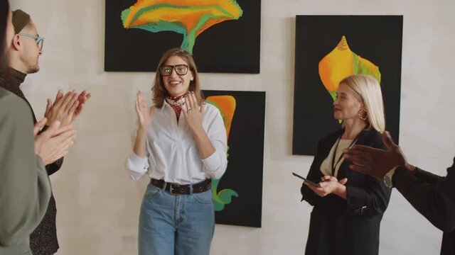 Young happy female artist saying thanks to public while they giving applauds and then telling about art exhibition in gallery