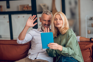 Smiling couple in sunglasses sitting on the sofa and having a video chat