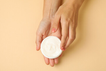 Cute female hands hold jar of cosmetic cream on beige background
