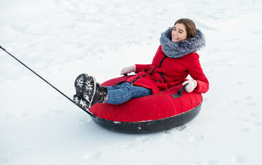 Fototapeta na wymiar Happy young girl are sliding on snow tubes winter day.