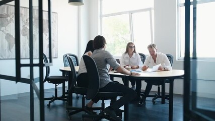 Young business people in formal clothes sitting by the table and working in the office with documents.