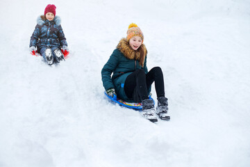 Fototapeta na wymiar Children are loving sledding down a steep hill during a snowly winter