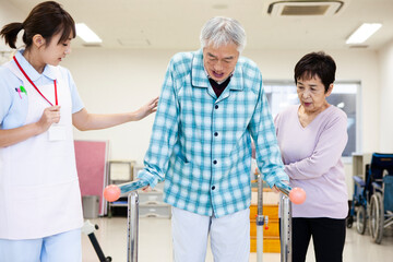歩行訓練を頑張る高齢男性とサポートをする奥さん、女性看護師