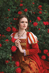 beautiful young woman with blue eyes in a dress in a medieval style is sitting in the garden with...