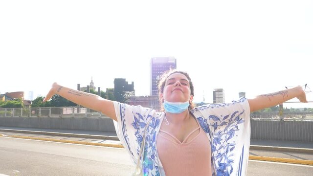 Slow motion young diverse mixed race woman outdoor spreading arms smiling celebrating freedom arms wide open wearing surgical mask unproperly
