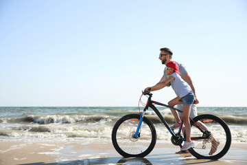 Fototapeta na wymiar Happy father teaching daughter to ride bicycle on sandy beach near sea