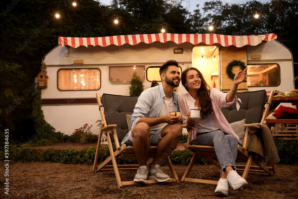 Wall mural Happy couple with cups resting near trailer. Camping season