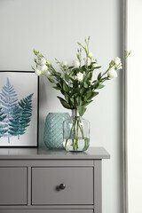 Composition with eustoma flowers in glass vase on grey cabinet indoors