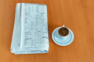 A cup of Turkish coffee and newspaper on the wooden table.