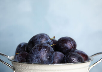 Delicious ripe plums in colander on light background, closeup. Space for text