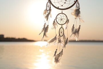 Beautiful handmade dream catcher near river at sunset. Space for text