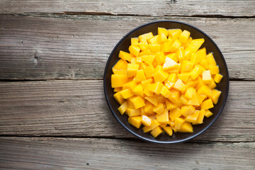Diced mango in a black plate on old wood. Top view.