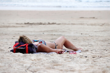 Woman sunbathing on a beach lying on sand. Tanned female body, beach vacation, relax and leisure by the sea