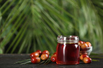 Palm oil in glass jar, tropical leaf and fruits on wooden table. Space for text