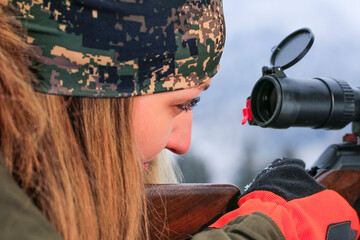 A young hunter woman on hunt looks into the rifle a waiting for wild animal.
