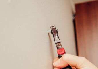Close up view of person hand removing old plastic dowel, nylon wall plug from drywall with pliers...
