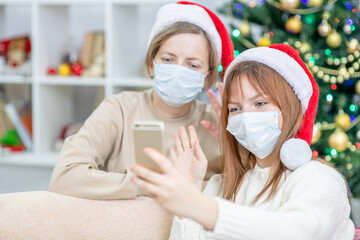 Happy family wearing Christmas hats, take video calls during coronavirus pandemic, with Christmas tree on the background. Coronavirus and Christmas concept