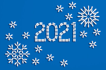 Medical concept congratulations on the year 2021. A lot of pills scattered on a blue background in the form of the number 2021 and snowflakes. 3D illustration