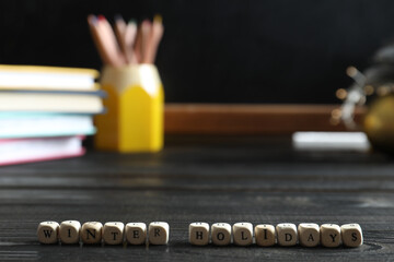 Cubes with phrase Winter Holidays on black wooden table in classroom. Space for text