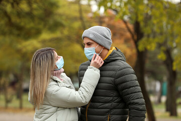 Couple in medical masks outdoors on autumn day. Protective measures during coronavirus quarantine