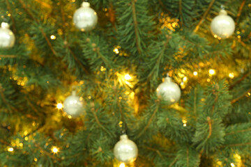 Fototapeta na wymiar Blurred view of glowing fairy lights and beautiful baubles on Christmas tree