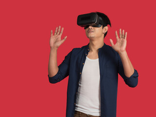 Young Asian man wearing casual clothes with virtual reality, VR  headset or 3d glasses playing game on red background.