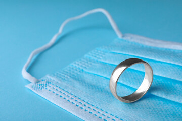 Wedding ring and medical mask on light blue background, space for text. Divorce during coronavirus...
