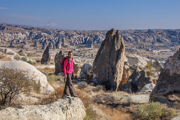 A girl in bright clothes, standing on a stone, looks at a beautiful landscape in Cappadocia. Turkey