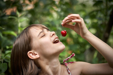 Portrait of laughing little girl eating cherries in the garden