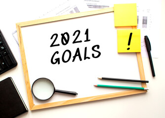 2021 GOALS text is written on a white office board. Work table with office supplies.