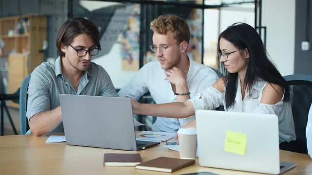 Modern young business people in glasses sitting by the table with laptop on it and working together. Guy giving document to the woman.