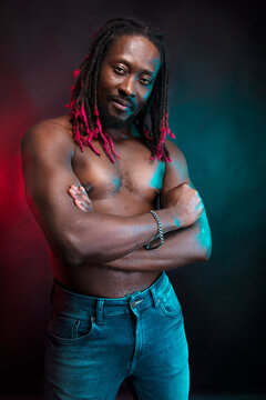 A black man in a sports uniform, with a naked torso. Hairstyle, African braids. Photo in the studio, black background.