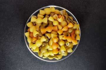 Italian pasta on a glass plate. Multi-colored pasta. Black background. Advertising concept with copy space for customized text.