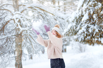 A young woman in a knitted hat with a pompom, mittens and a warm sweater plays with the snow