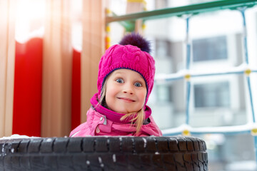 Portrait of cute adorable caucasian little happy blond kid girl enjoy having fun playing at outdoor kindergarten or yard playground on bright cold sunny winter day. Outside children play activities