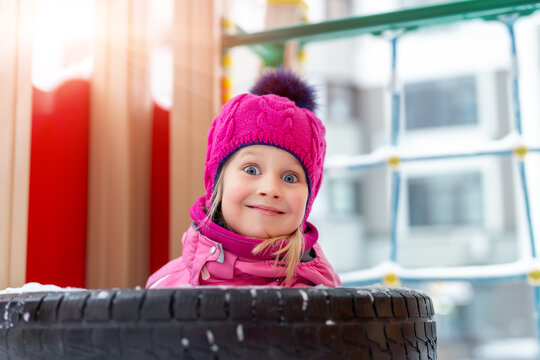 Portrait Of Cute Adorable Caucasian Little Happy Blond Kid Girl Enjoy Having Fun Playing At Outdoor Kindergarten Or Yard Playground On Bright Cold Sunny Winter Day. Outside Children Play Activities