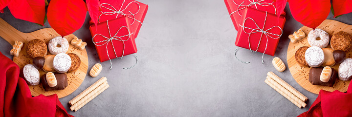 Traditional Spanish Christmas sweets turron, polvorones, mantecados with Christmas decor and red gift boxes on grey table top, copy space, web banner © Maria Shchipakina