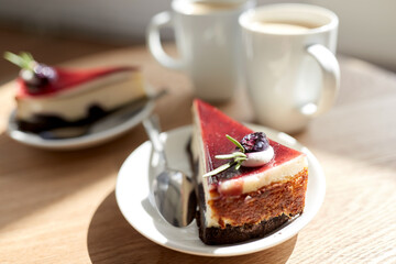 food, junk-food, culinary, baking and holidays concept - piece of delicious cherry chocolate layer cake on saucer with spoon on wooden table