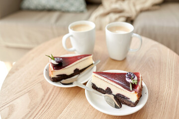 food, junk-food, culinary, baking and holidays concept - pieces of delicious cake on saucers with spoons and coffee cups on wooden table