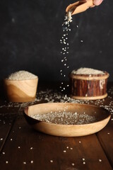 Sesame seed dripping down from spoon into wood plate, with black background.