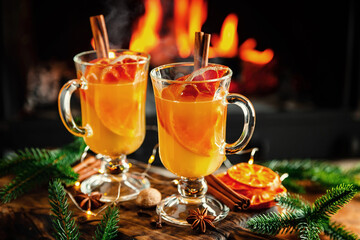 Mulled cider glasses on the background of fireplace fire. Hot mulled spiced apple cider cocktail for winter or autumn time.