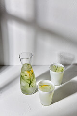 drink, detox and diet concept - glasses with fruit water or lemonade with lemon and cucumber dropping shadows on white surface