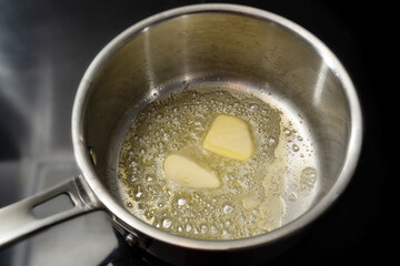 Melting butter in a stainless steel saucepan on the black stove, cooking concept, selected focus - obrazy, fototapety, plakaty