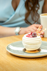 Sweet white cupcake with berries on the plate at the table on a woman's background with a cup of coffee in a cafe