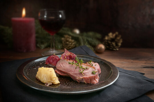 Festive holiday meal from duck breast with mashed parsnip and figs, red wine, candle and Christmas decoration against a rustic dark background, copy space, selected focus