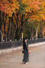 Young woman in black hat and jacket in city park in autumn