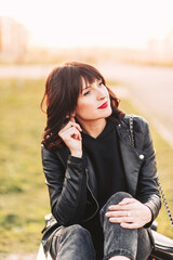 Pensive girl in a black jacket sits on a bench in the street in the evening