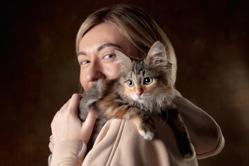 A small purebred kitten sitting on the shoulder of a young woman isolated on colored background....